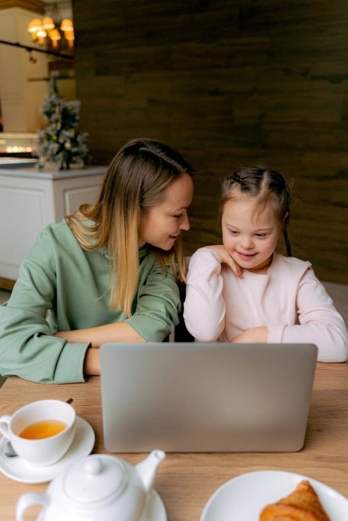 Mother and daughter with Down syndrome enjoy time together using a laptop. Cozy indoor setting.